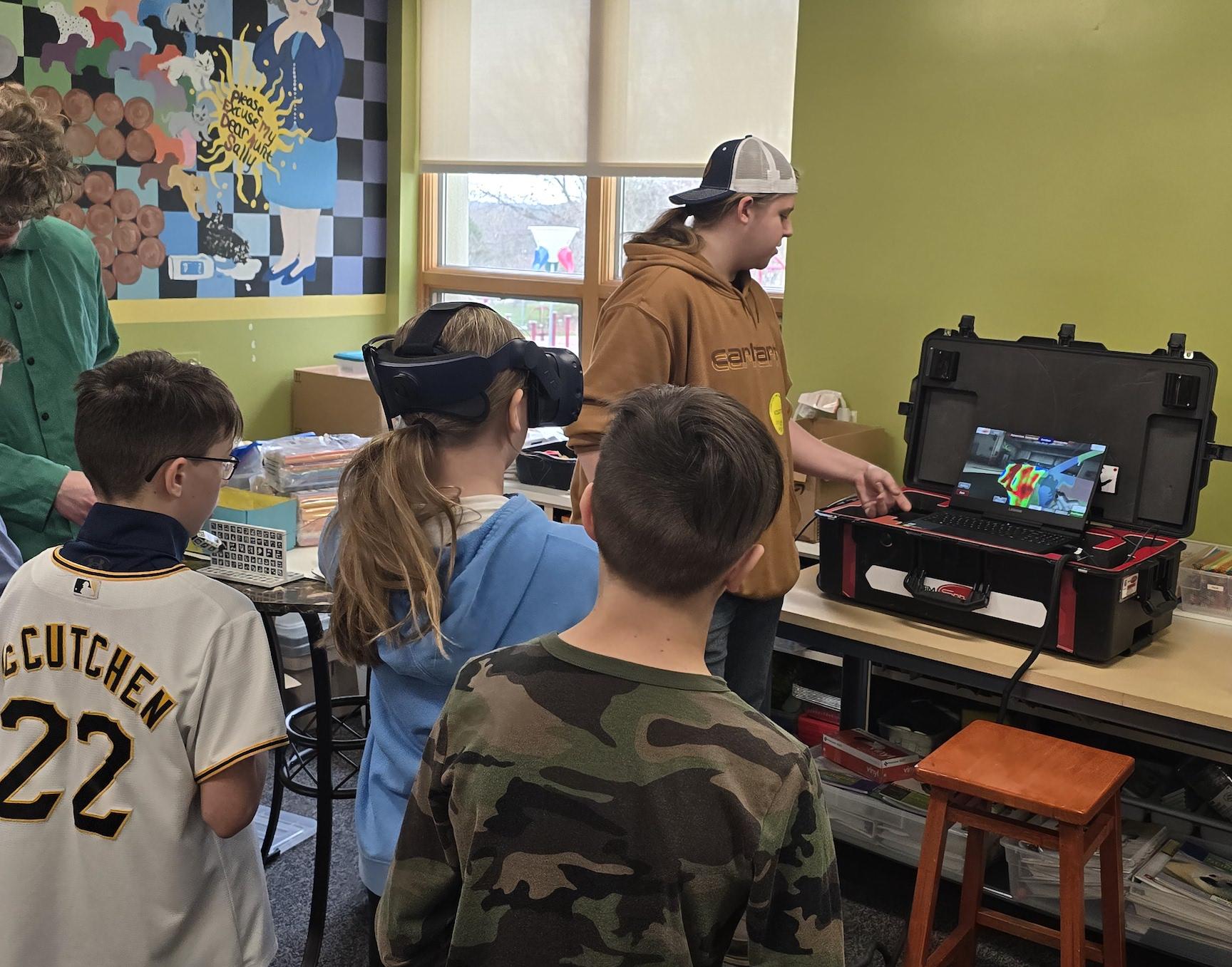 Harrison Park students Charles Spreyne and Abel Busbey watch Alana Hutchison use a virtual reality program to simulate painting cars while Penn-Trafford High School/CWCTC student, Nathan Lasitis, supervised the station